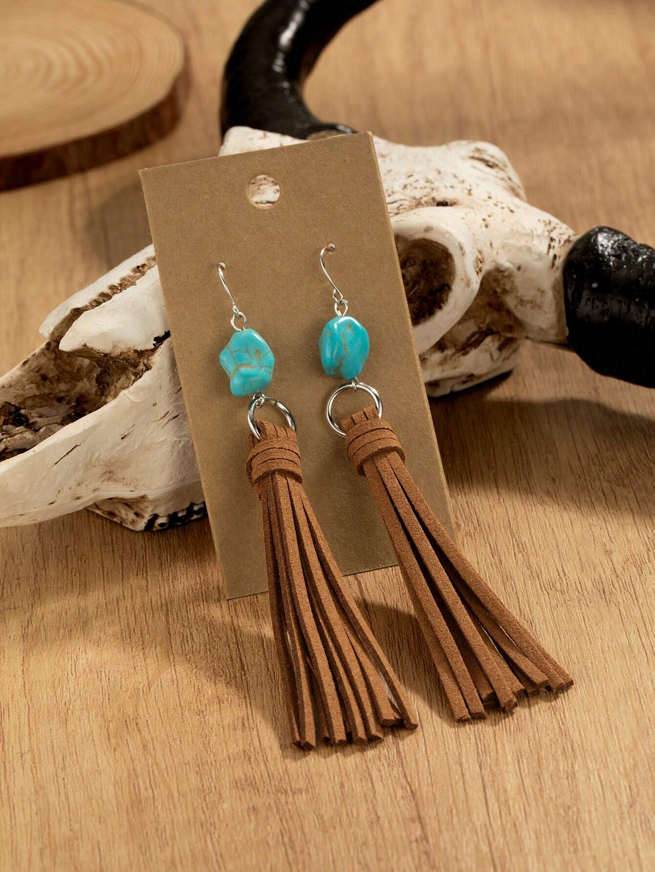Turquoise bead and brown tassel earrings on a wooden surface with a rustic background.