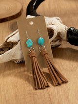 Turquoise bead and brown tassel earrings on a wooden surface with a rustic background.