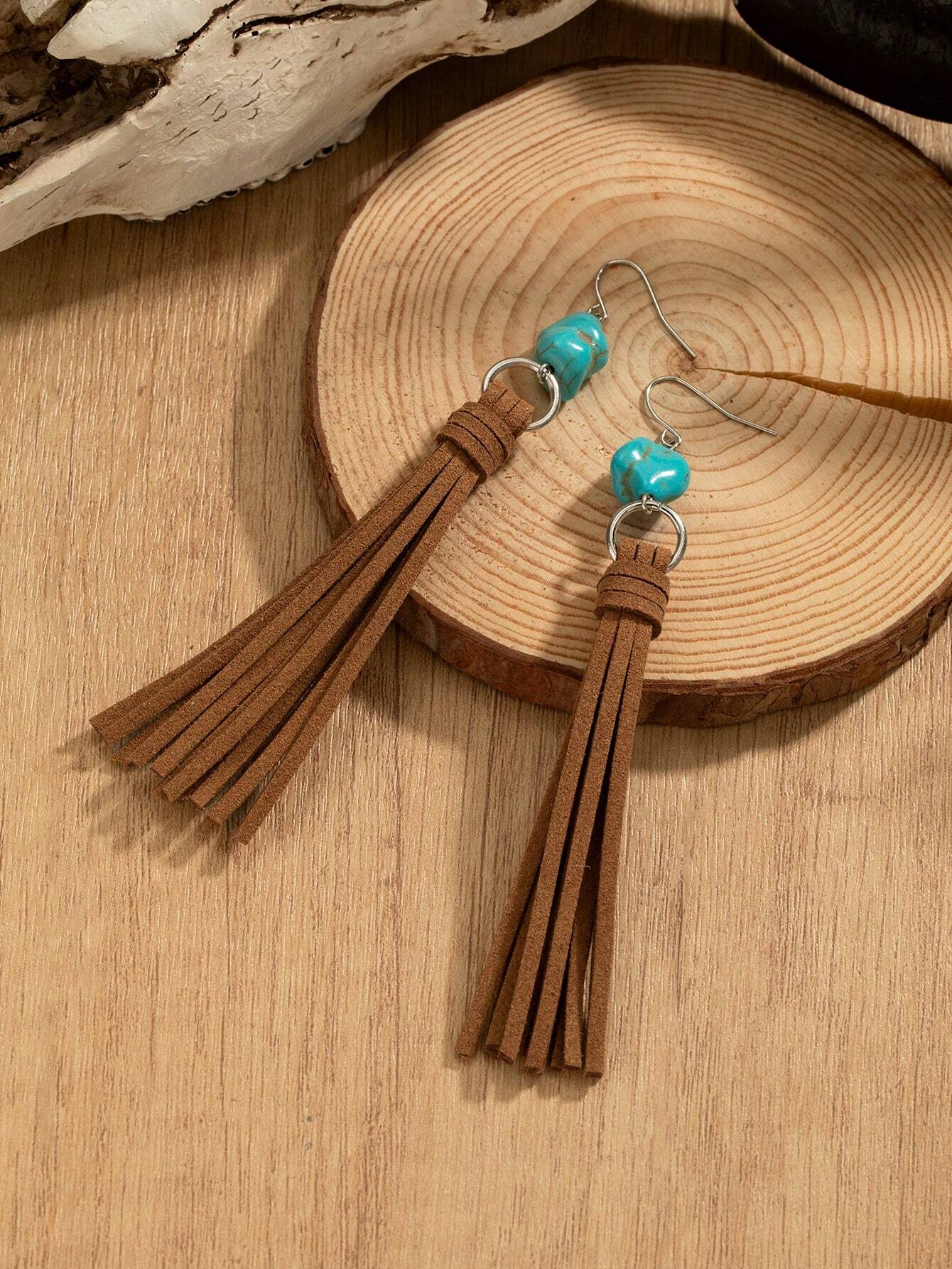 Brown tassel earrings with turquoise beads on a wooden surface