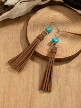 Brown tassel earrings with turquoise beads on a wooden surface