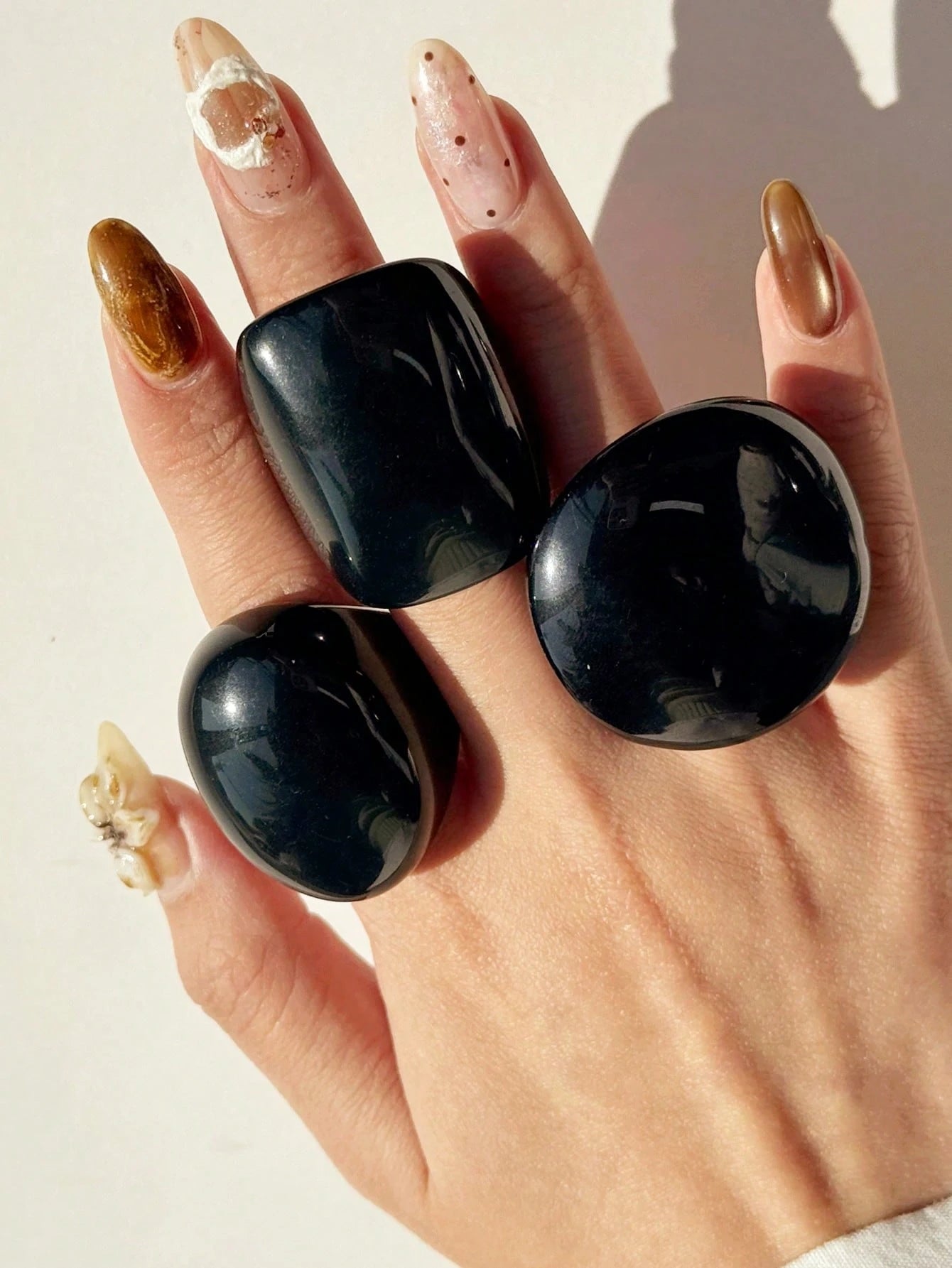 Hand wearing three black stone rings on a neutral background