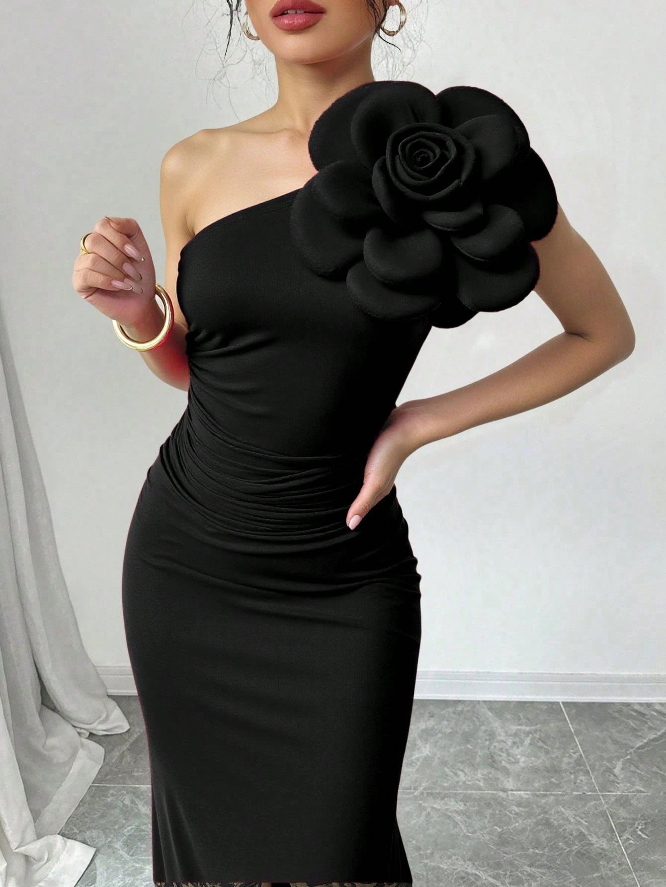 Black one-shoulder dress with a large floral embellishment on a plain background