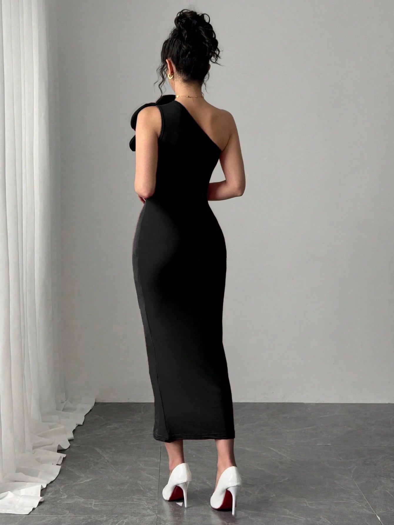 Woman wearing a black one-shoulder dress with white high heels in a minimalistic setting.