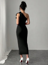 Woman wearing a black one-shoulder dress with white high heels in a minimalistic setting.