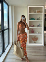 Woman in an orange and yellow striped outfit standing in a room with a large window and shelves.