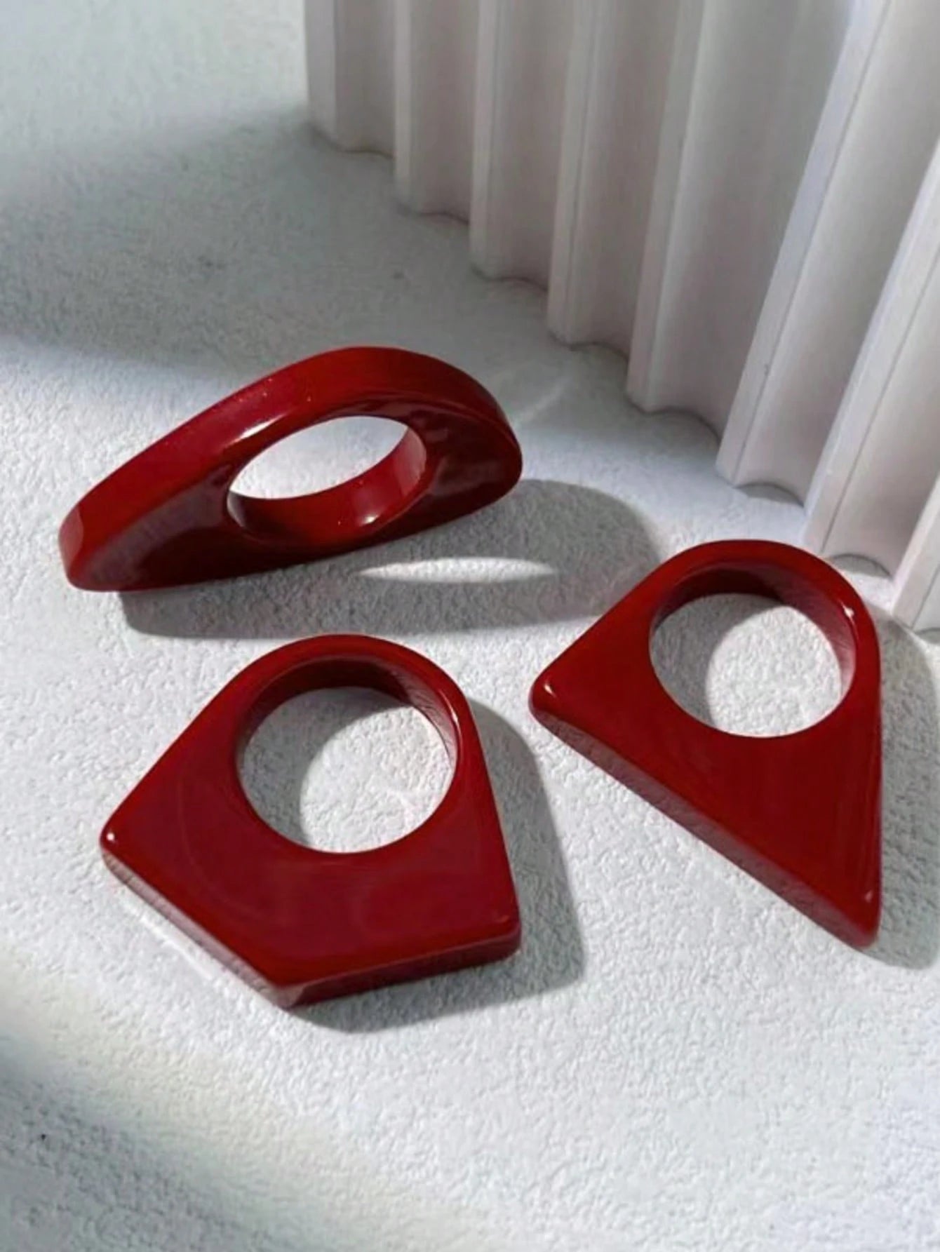 Three red plastic shapes on a textured white surface with a white curtain in the background.
