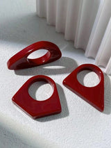 Three red plastic shapes on a textured white surface with a white curtain in the background.