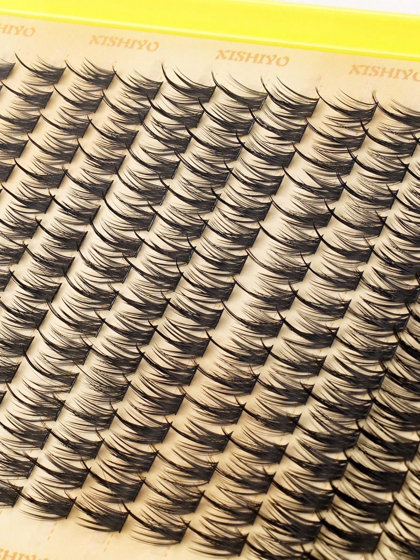 Close-up of a tray of false eyelash clusters on a beige card with the brand name KISHIYO printed repeatedly at the top.