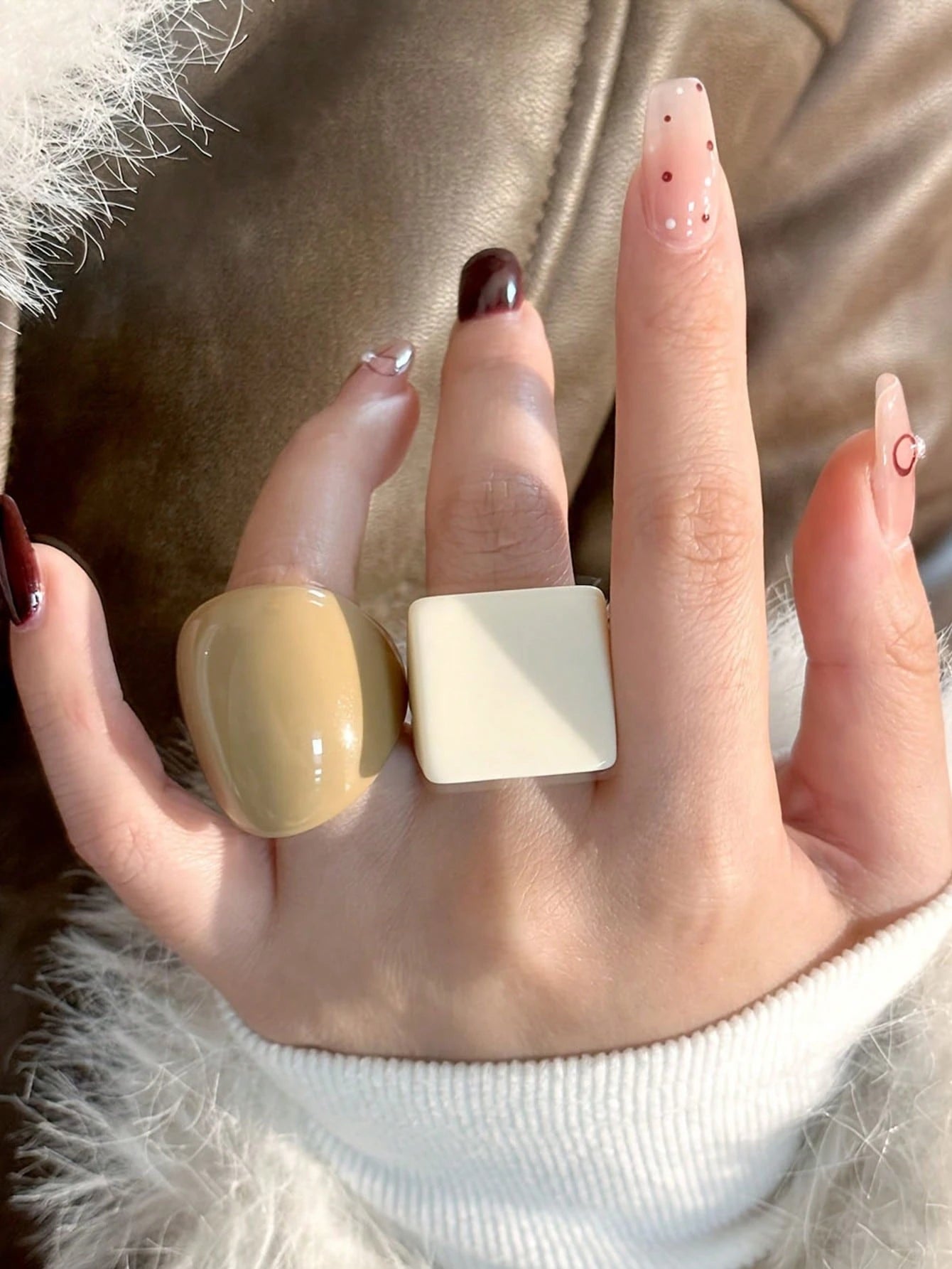 Hand wearing two large rings with a neutral background