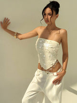 Woman wearing a white sequin top and white pants against a plain background