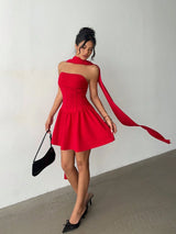 Woman in a red dress with a long train holding a black clutch against a neutral background