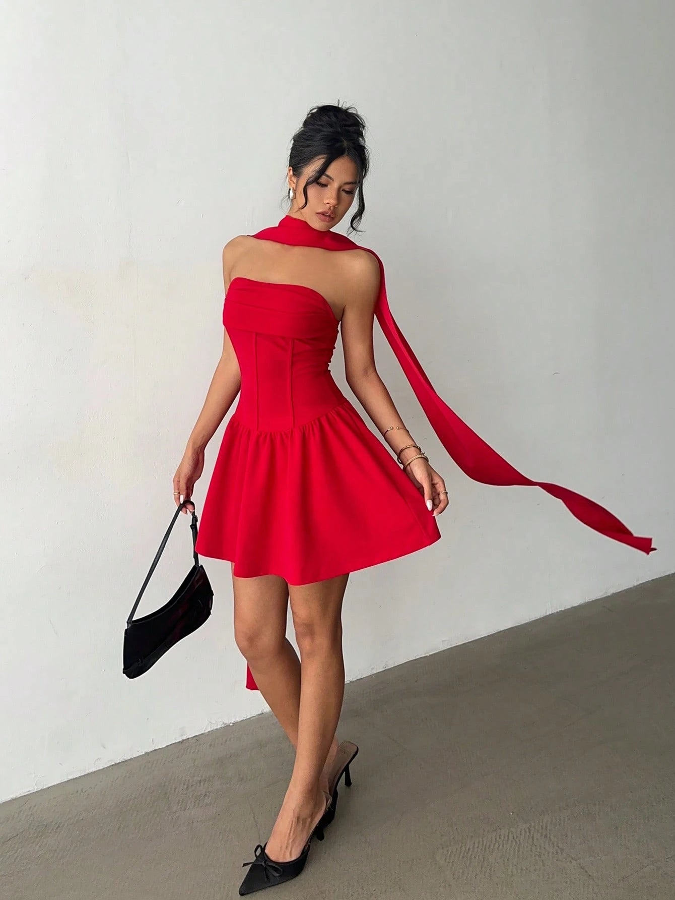 Woman in a red dress with a long train holding a black clutch against a neutral background