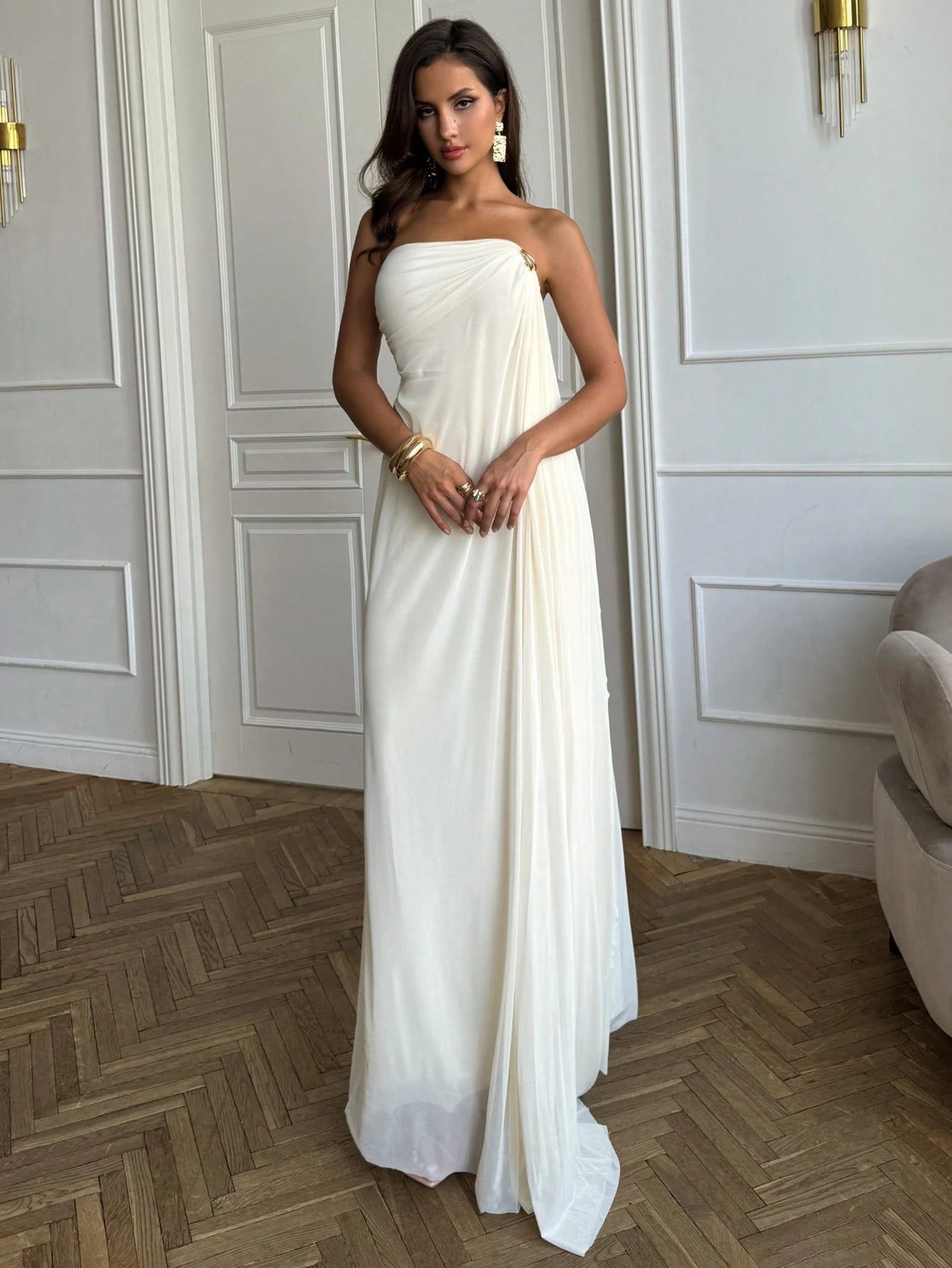 Woman wearing a strapless white gown in an elegant room with wooden flooring and white walls.