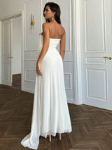 Woman in a white strapless gown standing in a room with wooden flooring and white walls.