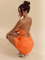 Woman wearing an orange dress with cut-out back on a beige background