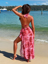 Woman in a pink floral dress standing on a beach with ocean and sky in the background