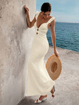 Woman in a white dress holding a straw hat by the ocean.
