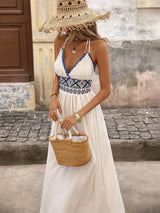 Woman in a white dress with blue patterns, holding a straw bag, standing on a street.