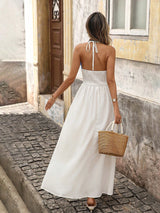 Woman in a white dress walking down a street holding a straw bag.
