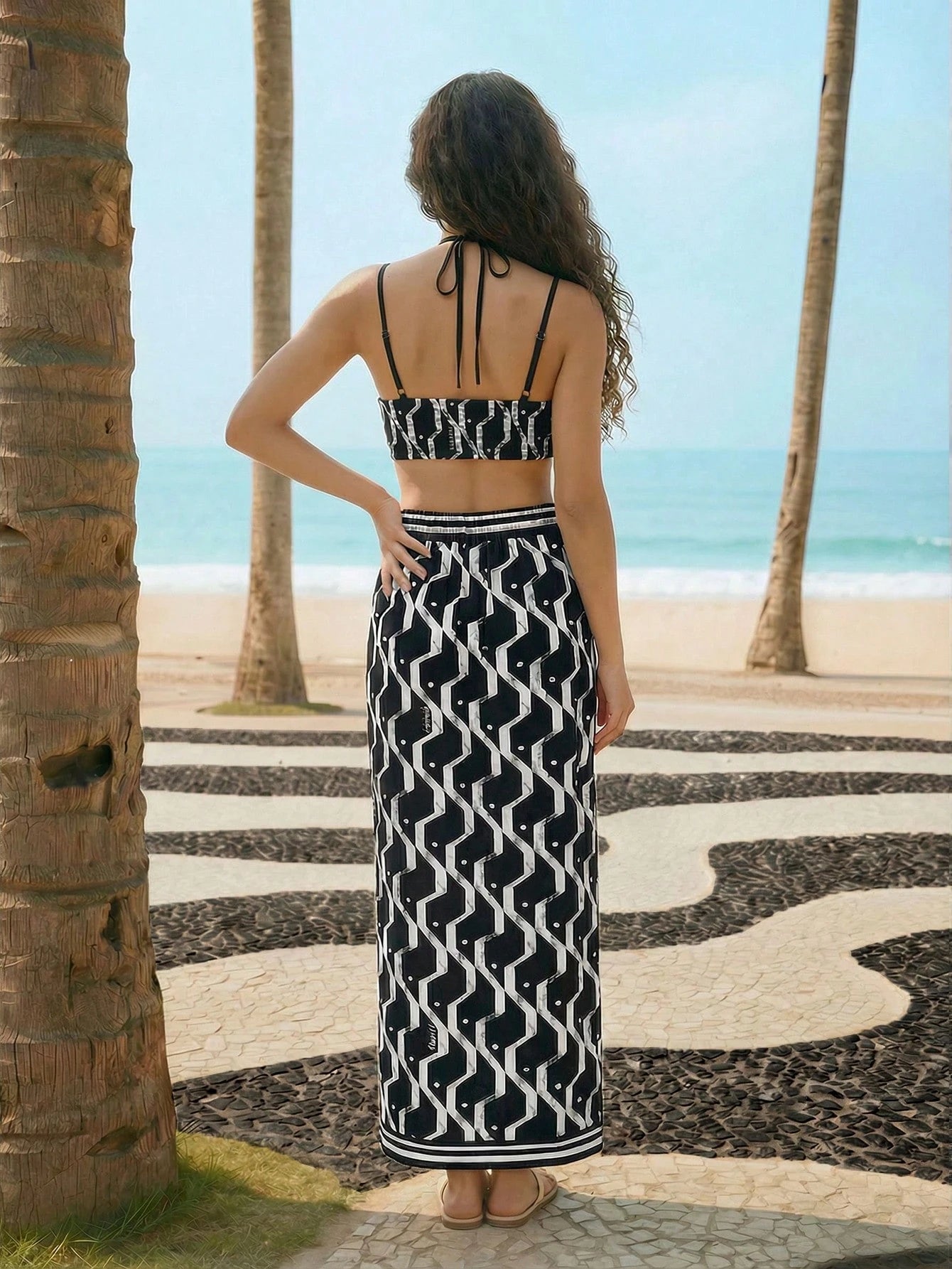 Woman in a black and white patterned dress standing on a beach with palm trees.