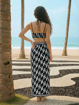Woman in a black and white patterned dress standing on a beach with palm trees.