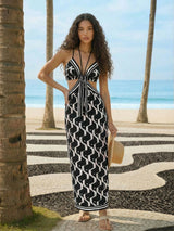 Woman in a black and white patterned dress standing on a beach with palm trees.