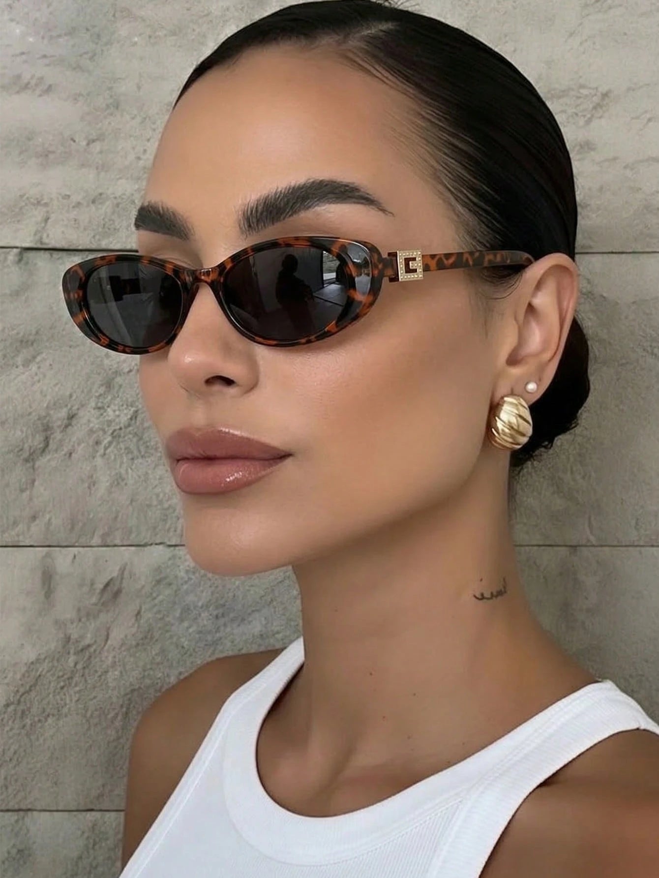 Woman wearing tortoiseshell sunglasses and gold earrings against a neutral background