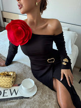 Woman in a black off-shoulder dress with a red flower and gold accessories on a bed.