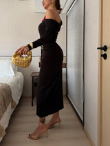 Woman in a black dress holding a gold handbag in a bedroom setting