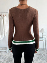 A woman viewed from the back wearing a fitted brown ribbed knit sweater with green and white striped trim at the hem and cuffs, paired with black pants in a bright indoor room.