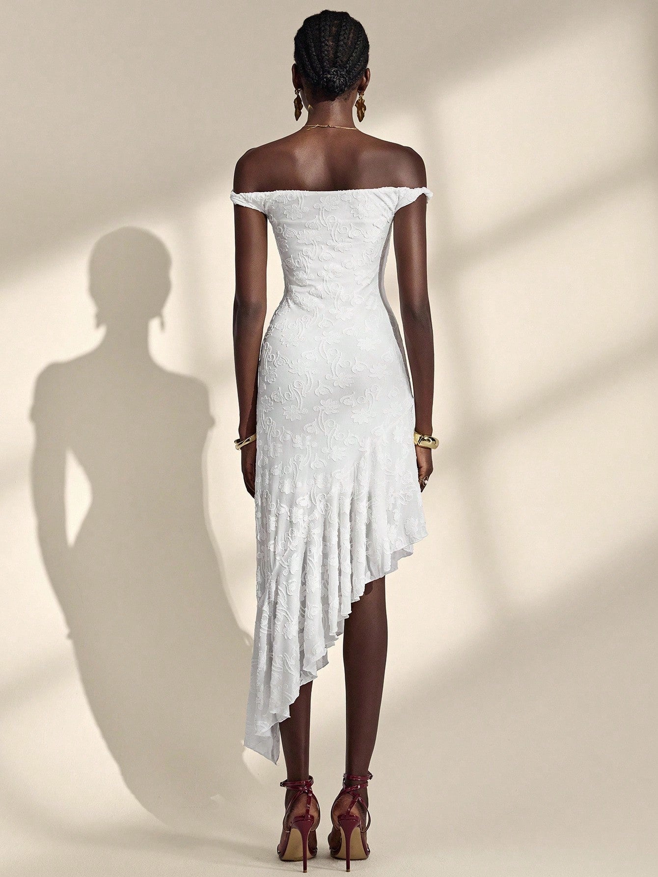 Woman wearing a white off-shoulder dress with a high-low hem on a beige background
