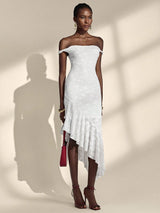 Woman wearing a white off-shoulder dress with ruffled details against a neutral background