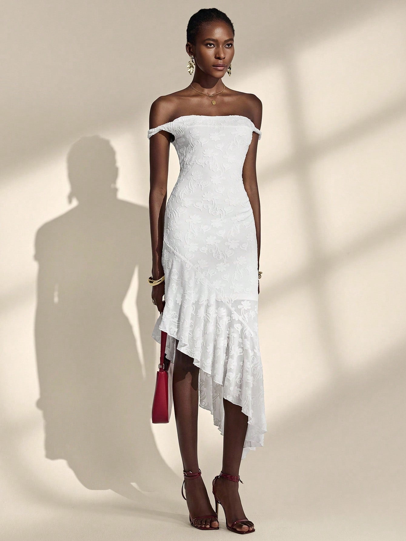 Woman wearing a white off-shoulder dress with ruffled details against a neutral background