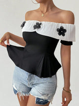 Person wearing a black and white off-shoulder top with floral details and denim shorts on a plain background