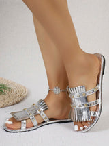 Silver fringe sandals worn on a foot with a neutral background