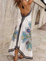 Woman wearing a white dress with colorful patterns standing against a stone wall.
