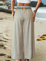 Person wearing light-colored wide-leg pants with a colorful waistband on a beach.
