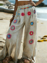 Beige pants with colorful floral embroidery on a beach.