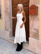 Woman in a white dress standing in front of a building entrance.