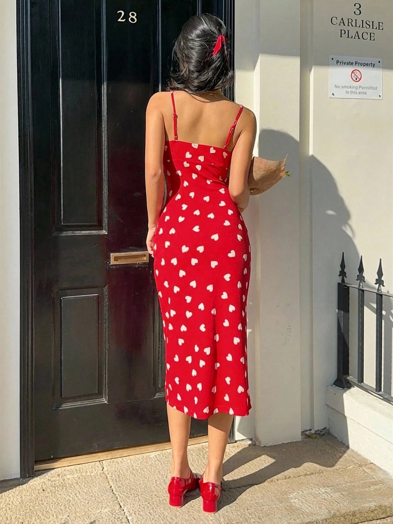Woman in a red dress with white heart patterns standing in front of a door.