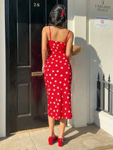 Woman in a red dress with white heart patterns standing in front of a door.