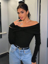 A woman posing in a black off-the-shoulder long-sleeve ribbed top and light blue jeans.