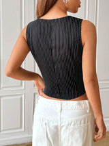 Person wearing a black pinstripe sleeveless top and white pants against a white paneled wall.