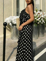 Woman in a black polka dot dress standing outdoors with flowers and a building in the background