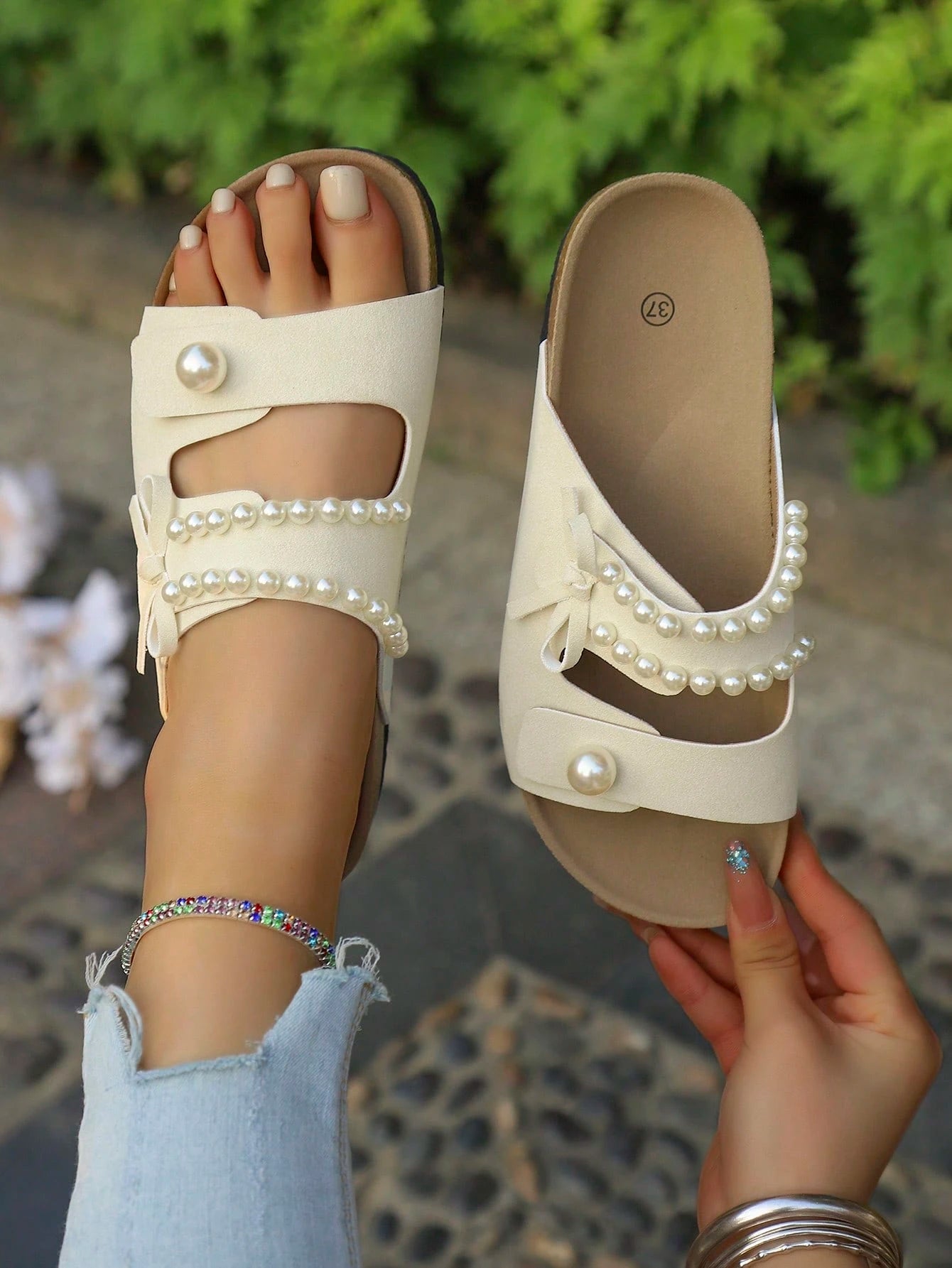 Beige sandals with pearl embellishments worn by a person on a patterned floor.