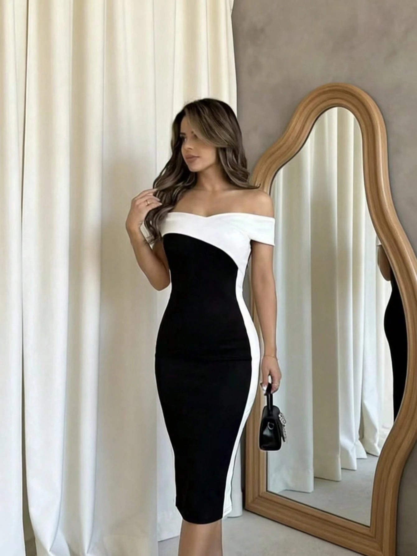 Woman in a black and white dress standing in front of a mirror with white curtains.