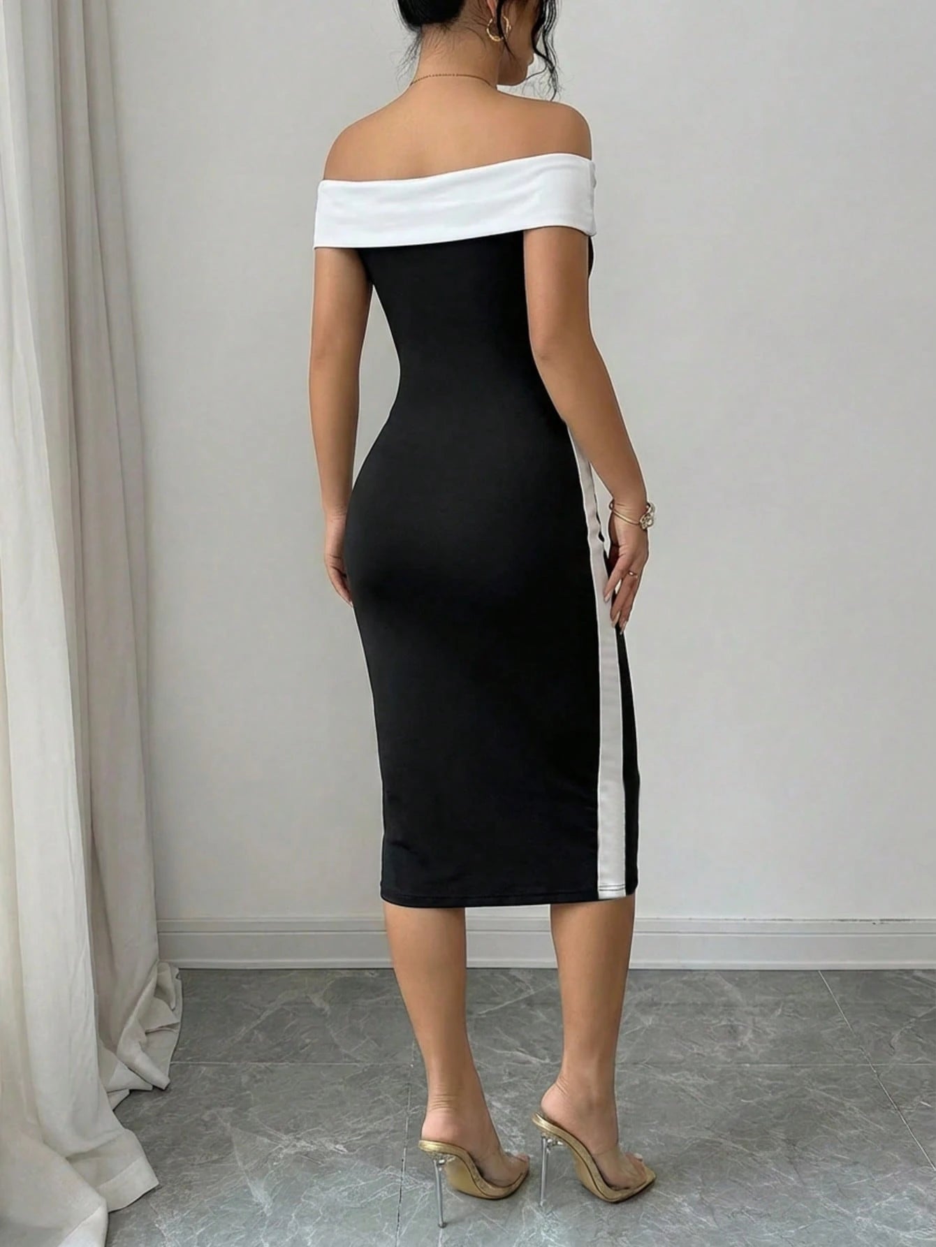 Woman wearing a black and white off-shoulder dress against a plain background