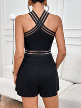 Person wearing a black romper with criss-cross straps in a room with white walls and furniture.