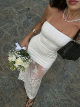Woman in a white off-shoulder dress with lace detailing holding a bouquet on a stone pavement.