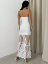 Woman wearing a white strapless dress with lace detailing in a minimal indoor setting.